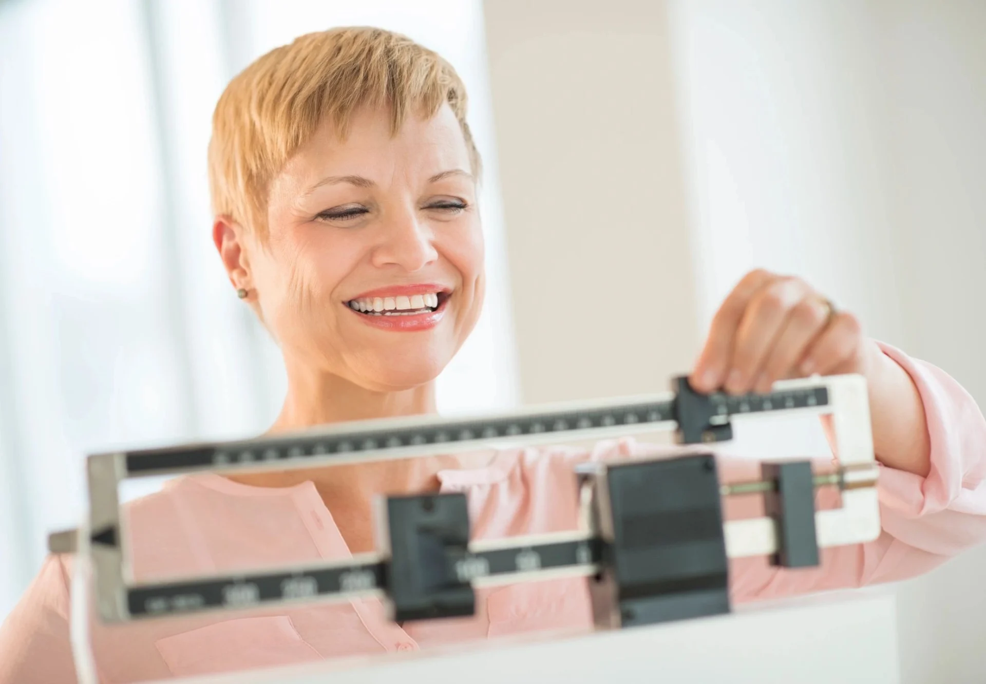 A woman smiles as she stands on the scale.